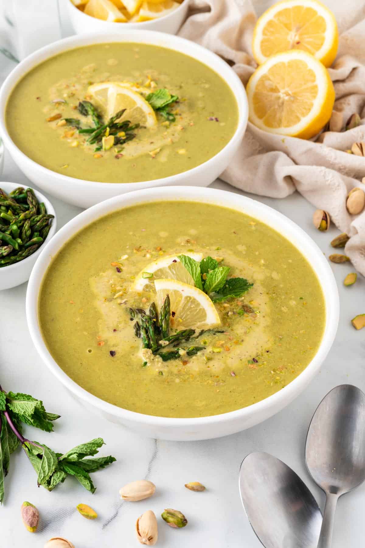 A picture of two bowls of asparagus soup with lemon, asparagus tips, and mint leaves for garnish.