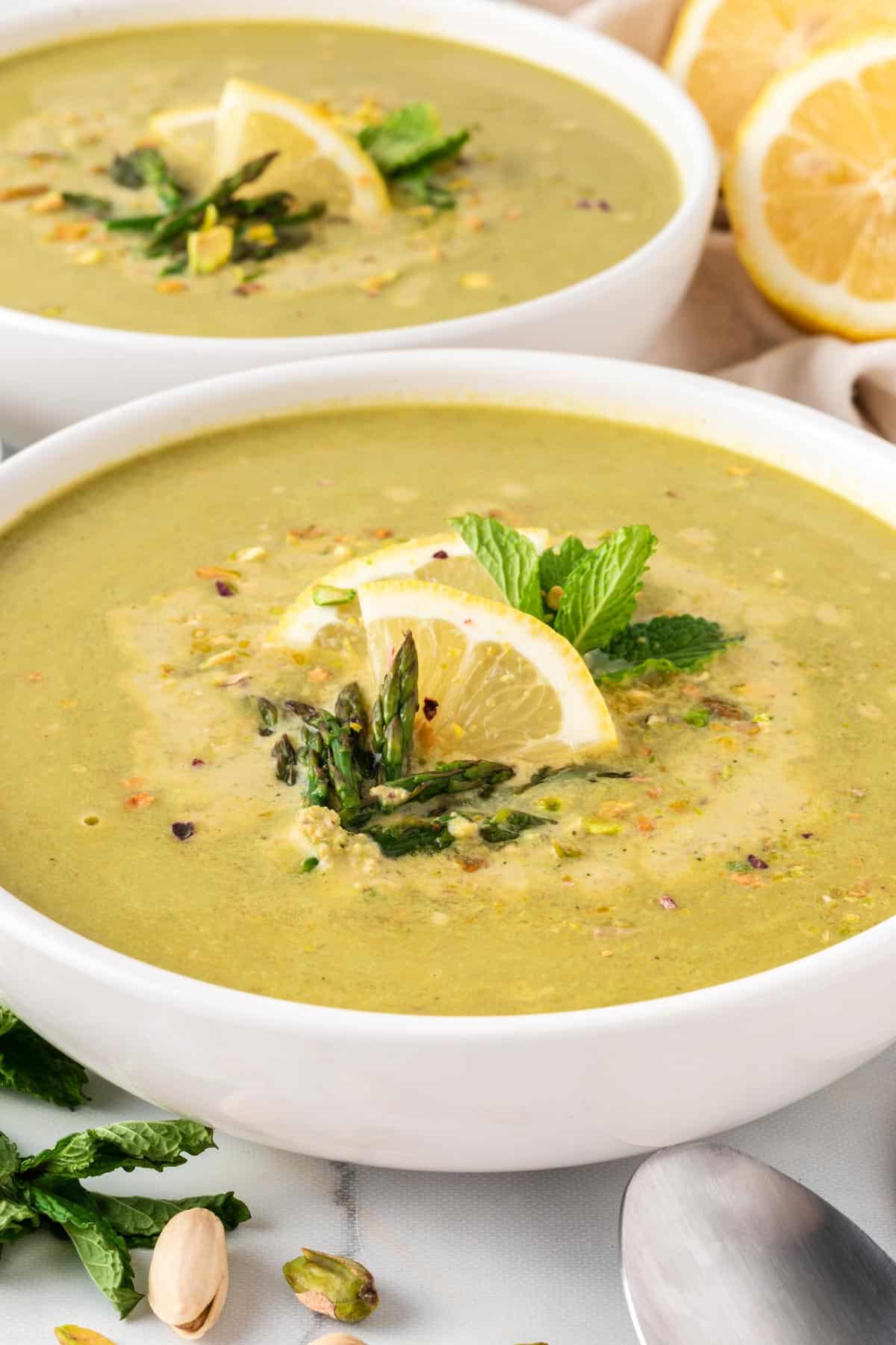 A close up picture of a bowl of asparagus soup with lemon slice on top.