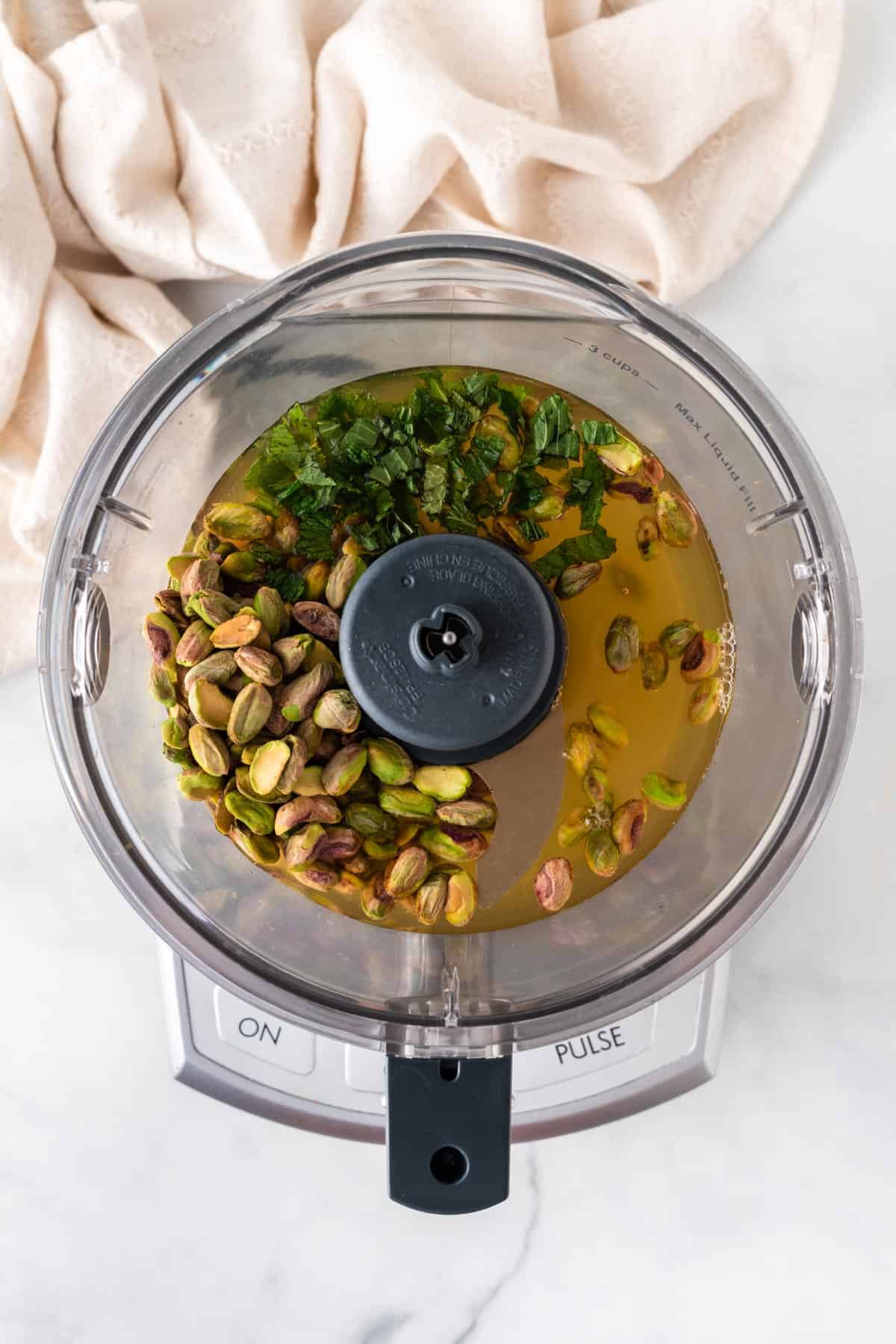A picture of pistachios, broth, and mint leaves in a food processor.