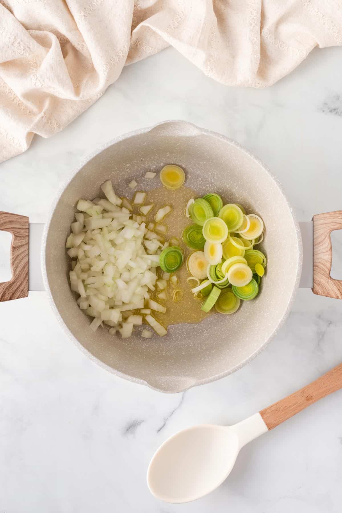 A picture of cooking onions and leeks in a oil in a pan with wooden handles.