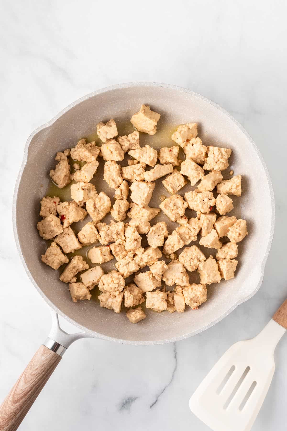 A picture of torn tofu being cooked in a white skillet.