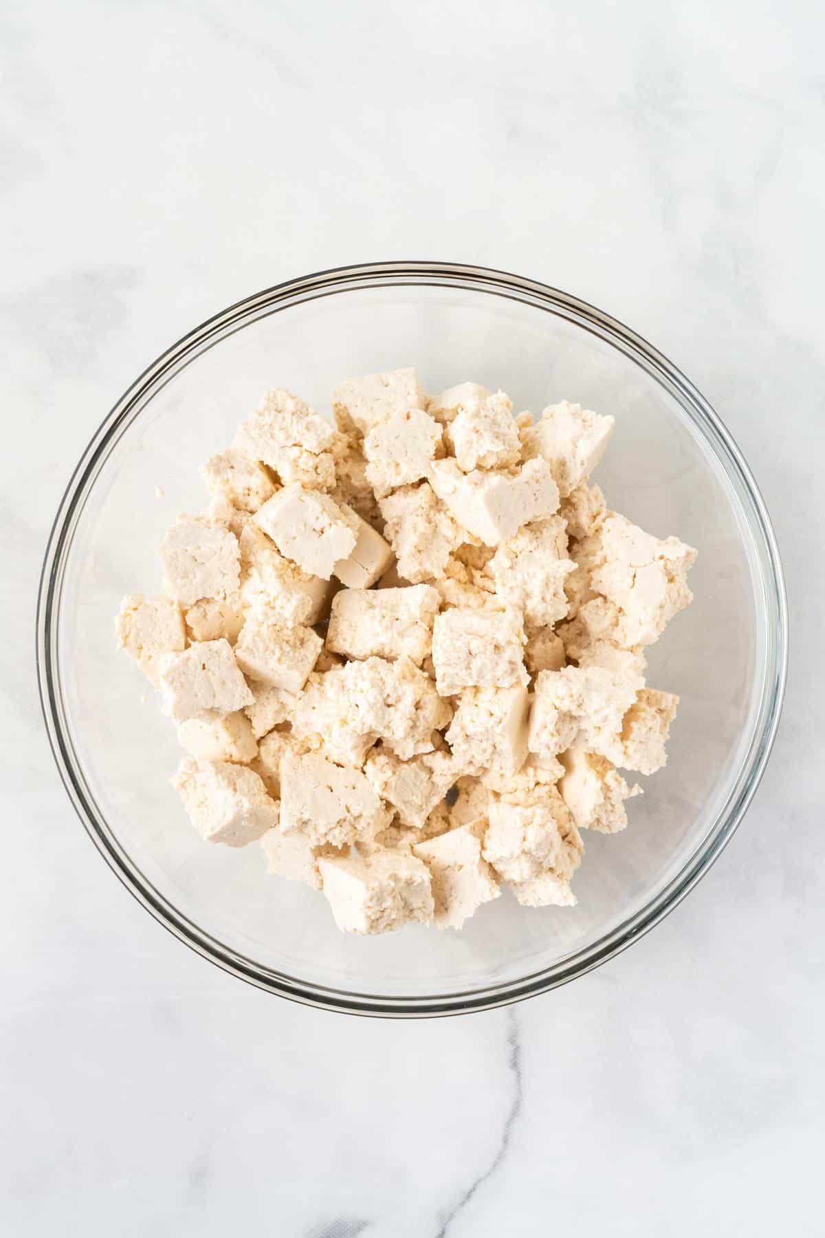A picture of torn tofu in a clear bowl.