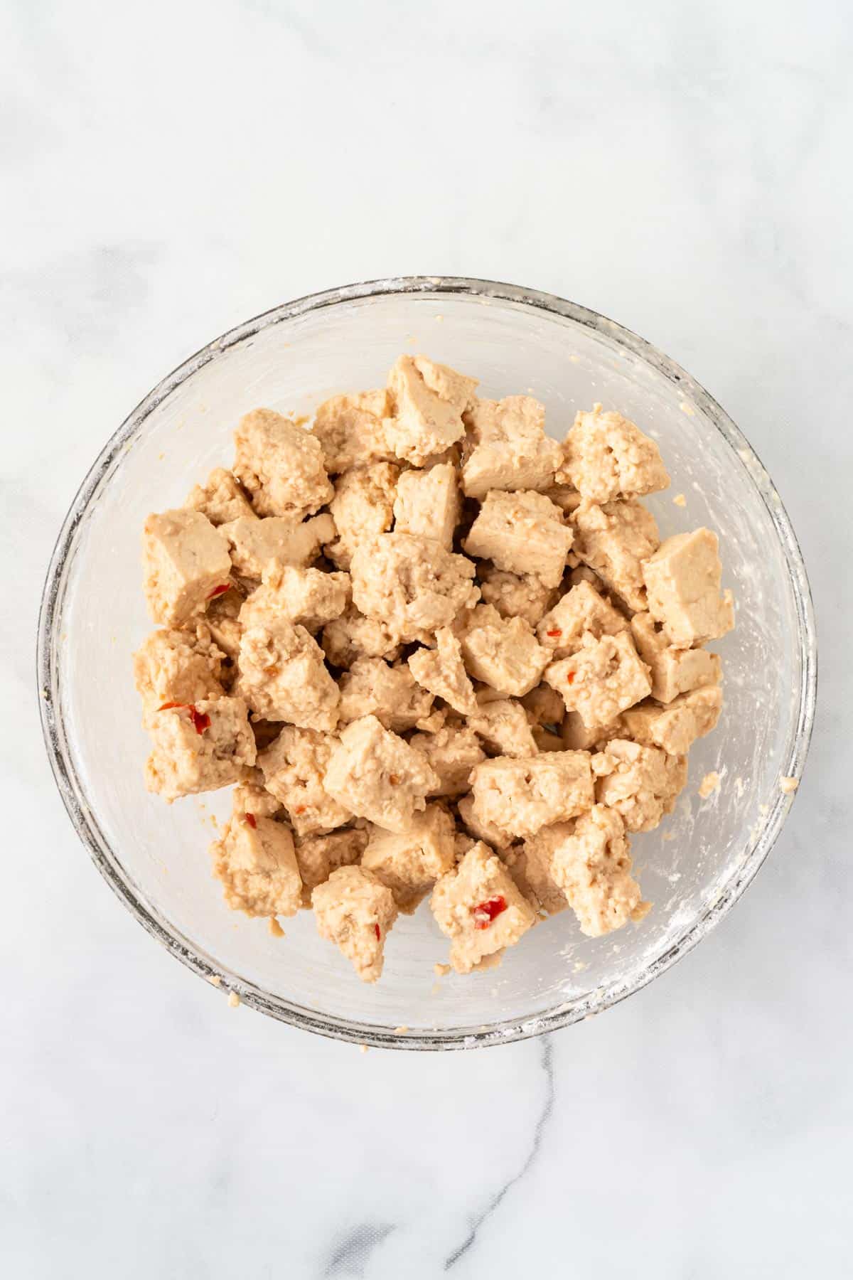 A picture of torn tofu coated in flour in a clear bowl.