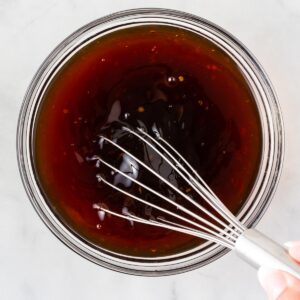 A square picture of whisking honey stir fry sauce in a clear bowl.
