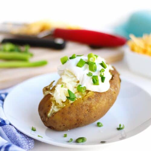 a picture of a baked potato topped with sour cream and chives on a white plate
