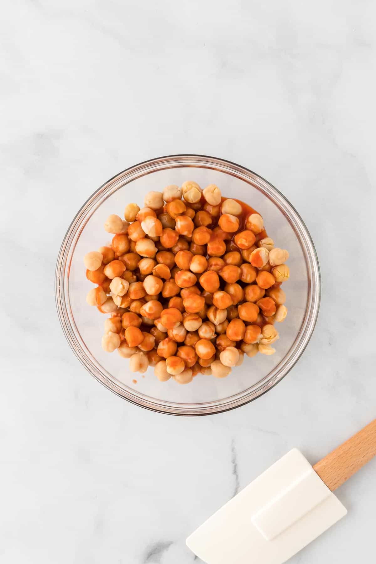 A picture of chickpeas with buffalo sauce on them in a glass bowl.