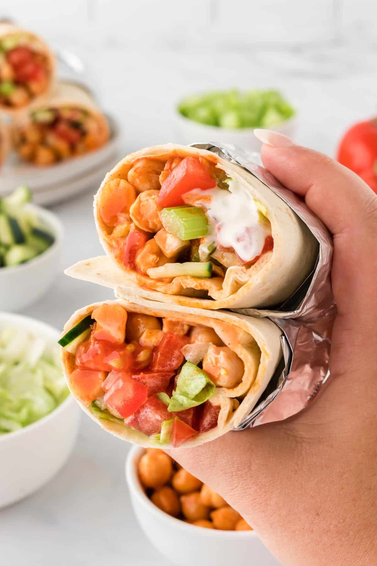 A photo of a stacked buffalo chickpea wrap being held by a hand.