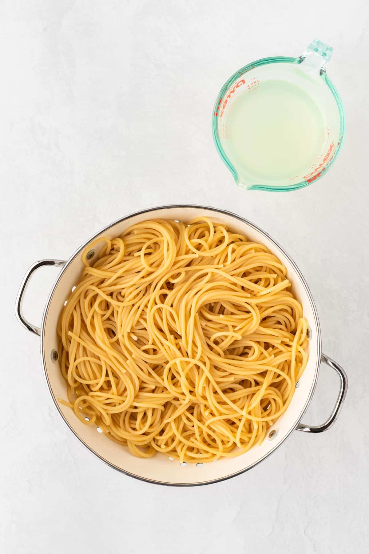A photo of strained spaghetti noodles in a colander with a measuring glass of pasta water.