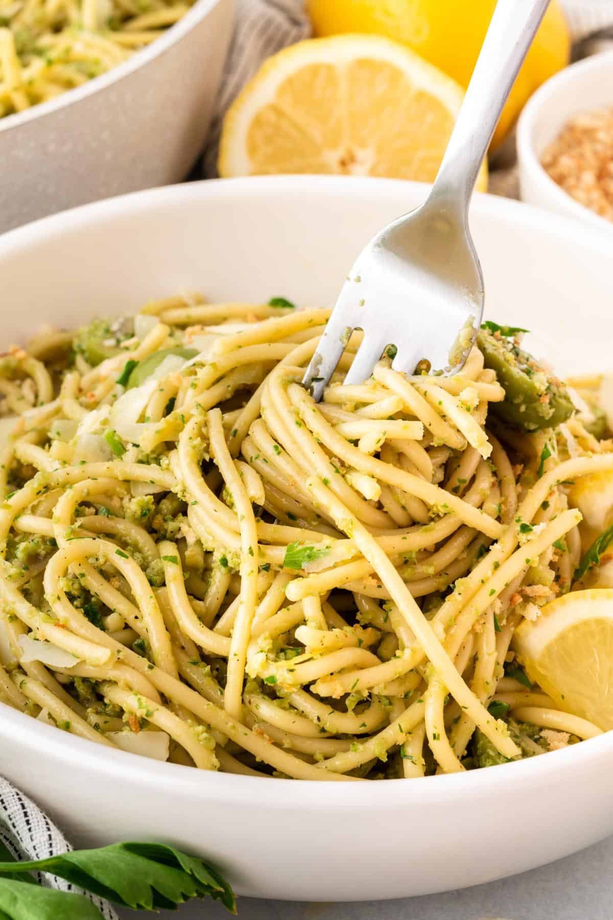 A photo of a fork twirling olive and herb spaghetti in a white bowl.