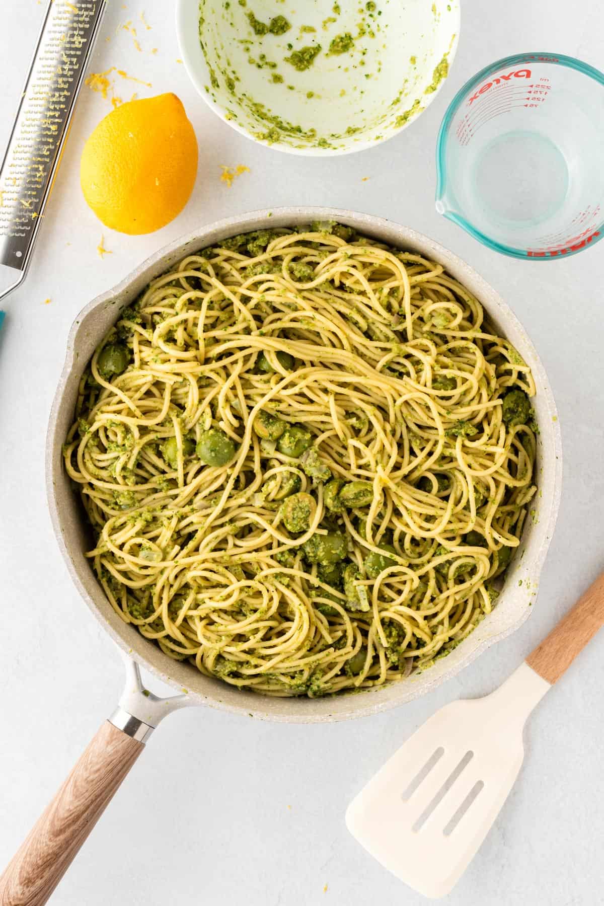 A picture of spaghetti with green olive sauce in a white skillet.