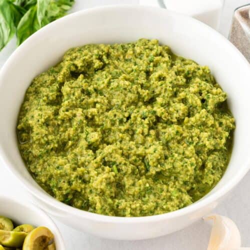 A square photo of green olive pasta sauce in a white bowl.