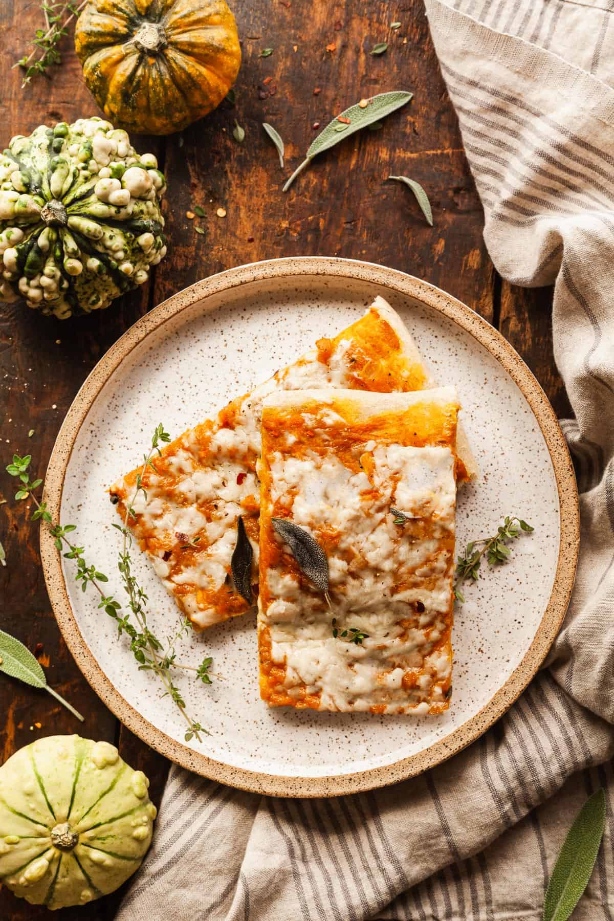 A photo of 2 square slices of pumpkin pizza on an oatmeal colored plate.