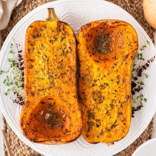 A square photo of roasted butternut squash halves on a white plate.