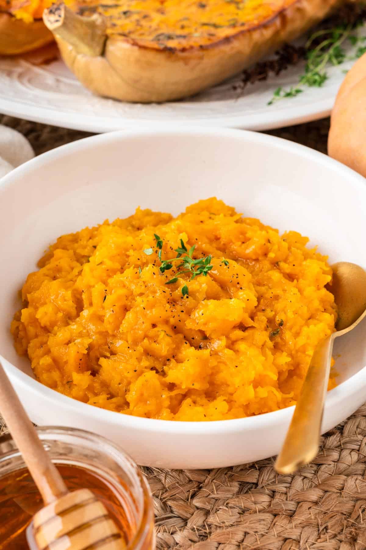 A photo of mashed butternut squash in a white bowl with a gold spoon.