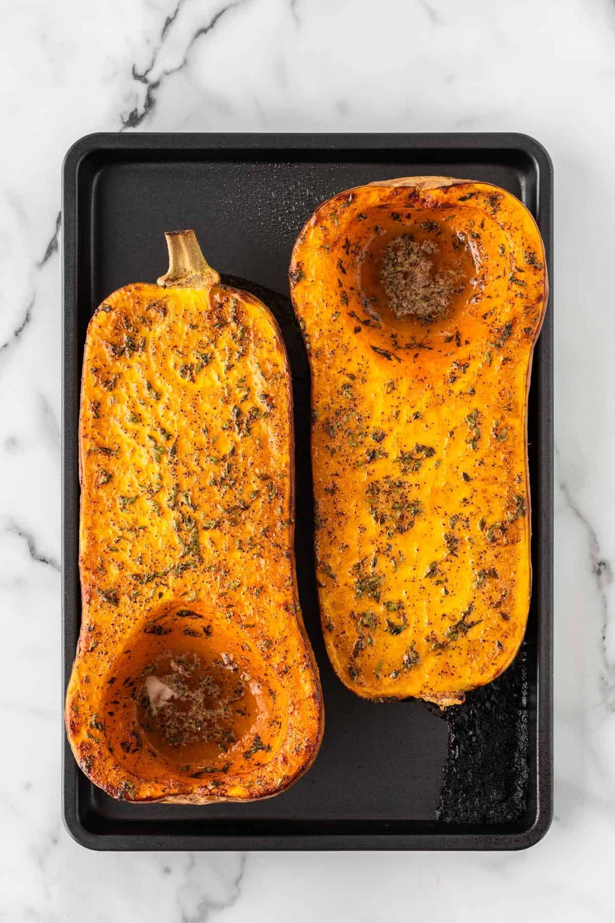 A photo of two roasted butternut squash halves next to each other on a baking sheet.