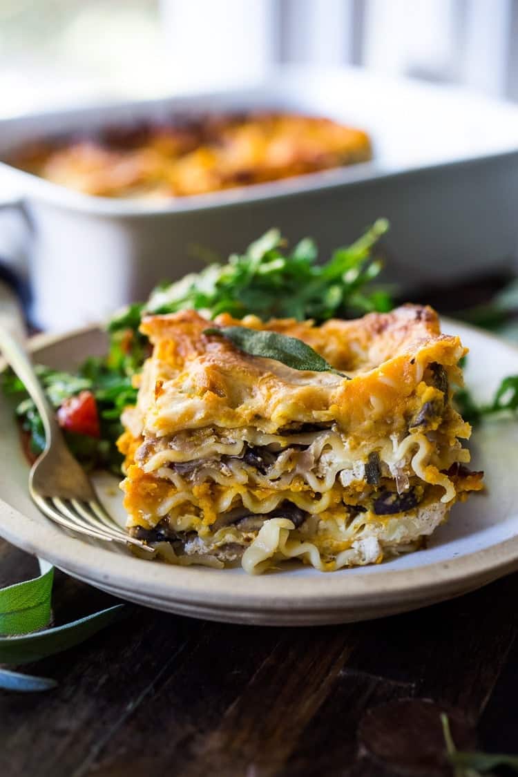 A photo of a slice of butternut squash lasagna on a plate with a fork.