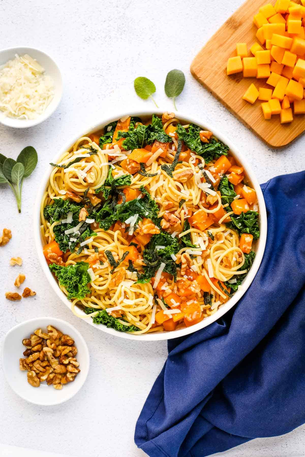 A photo of pasta with butternut squash and kale in a white bowl.