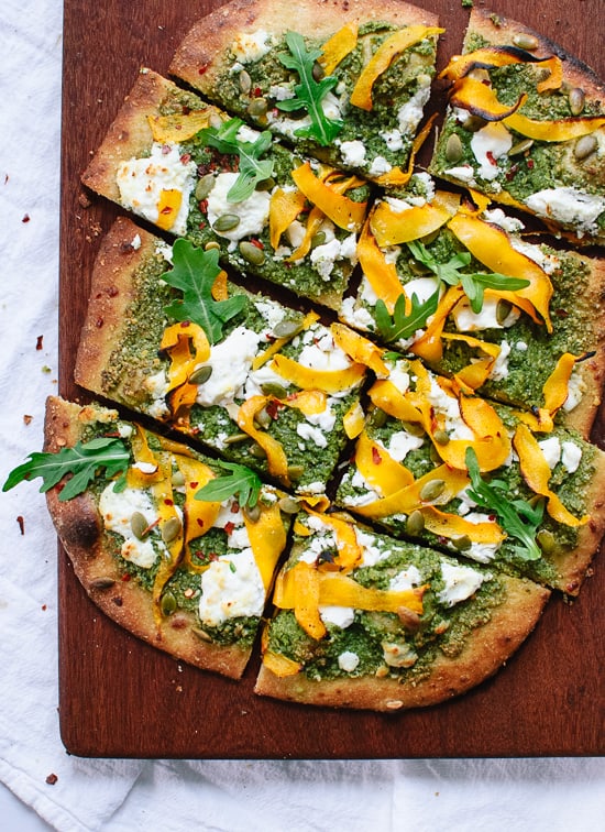 A photo of a pizza cut into square pieces with pesto, mozzarella, and butternut squash ribbons.