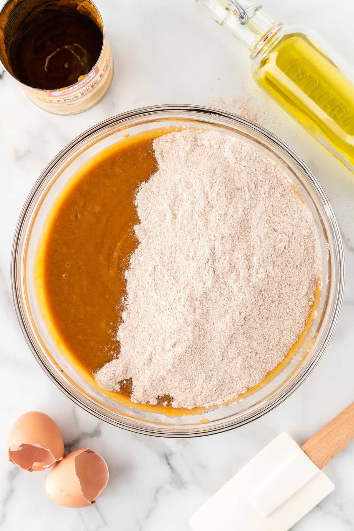 A photo of dry ingredients on top of wet ingredients for pumpkin bread.