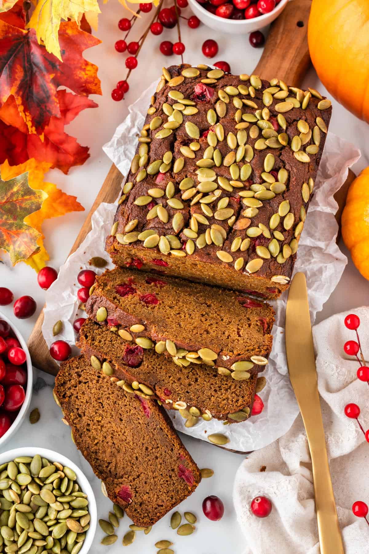 A photo of a loaf of pumpkin cranberry bread with a few slices at the front and pepitas on top.