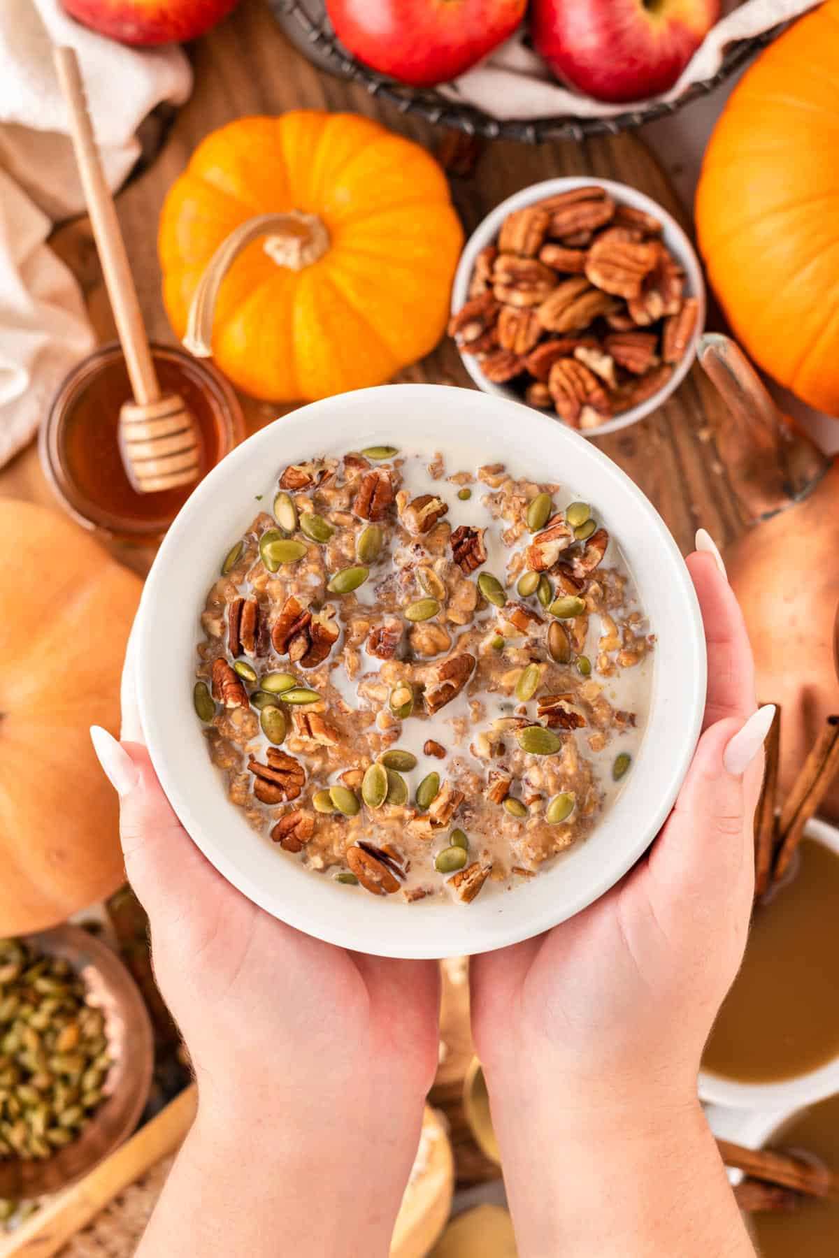 A photo of hands holding up a bowl of pumpkin oatmeal with nuts and milk.