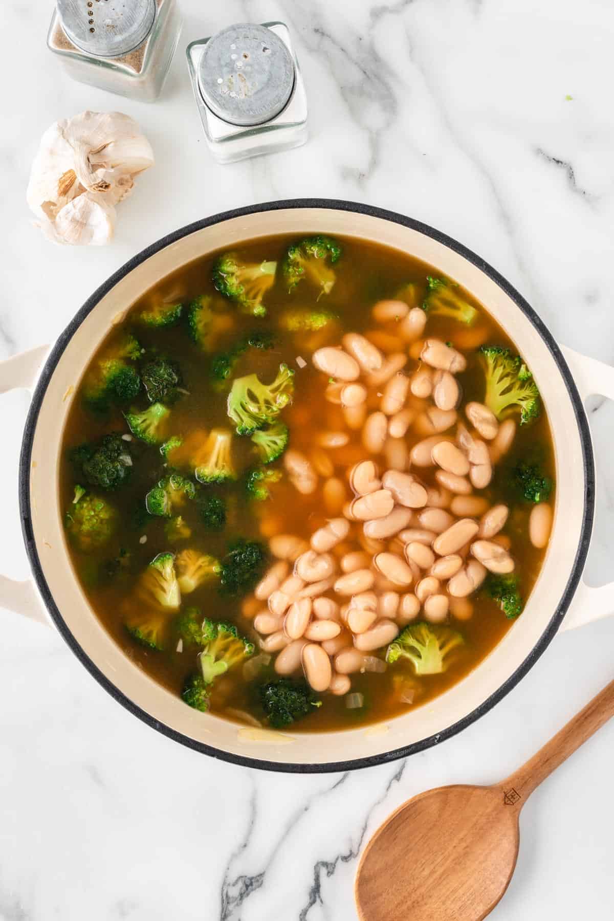 A photo of broccoli and white beans cooking in a pot with broth.