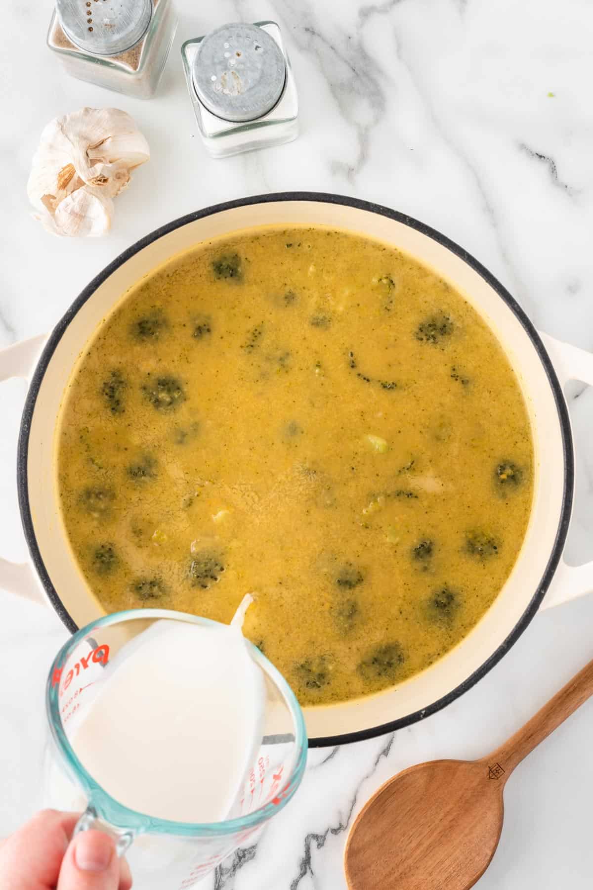 A photo of adding milk to broccoli cheddar soup.