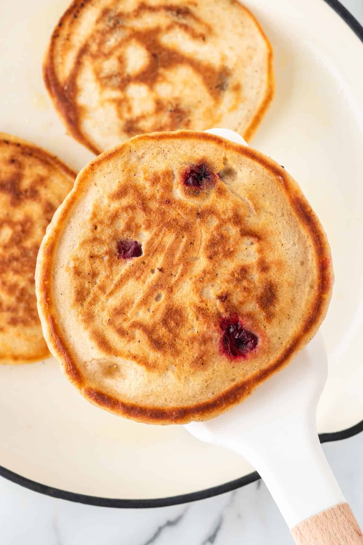 A photo of a cranberry pancake being held up with a white spatula.