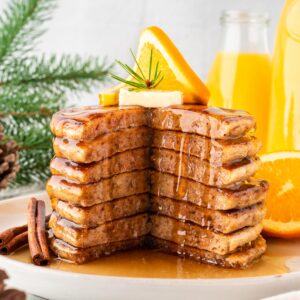 A photo of orange pancakes stacked with a slice cut out and maple syrup drizzling down.
