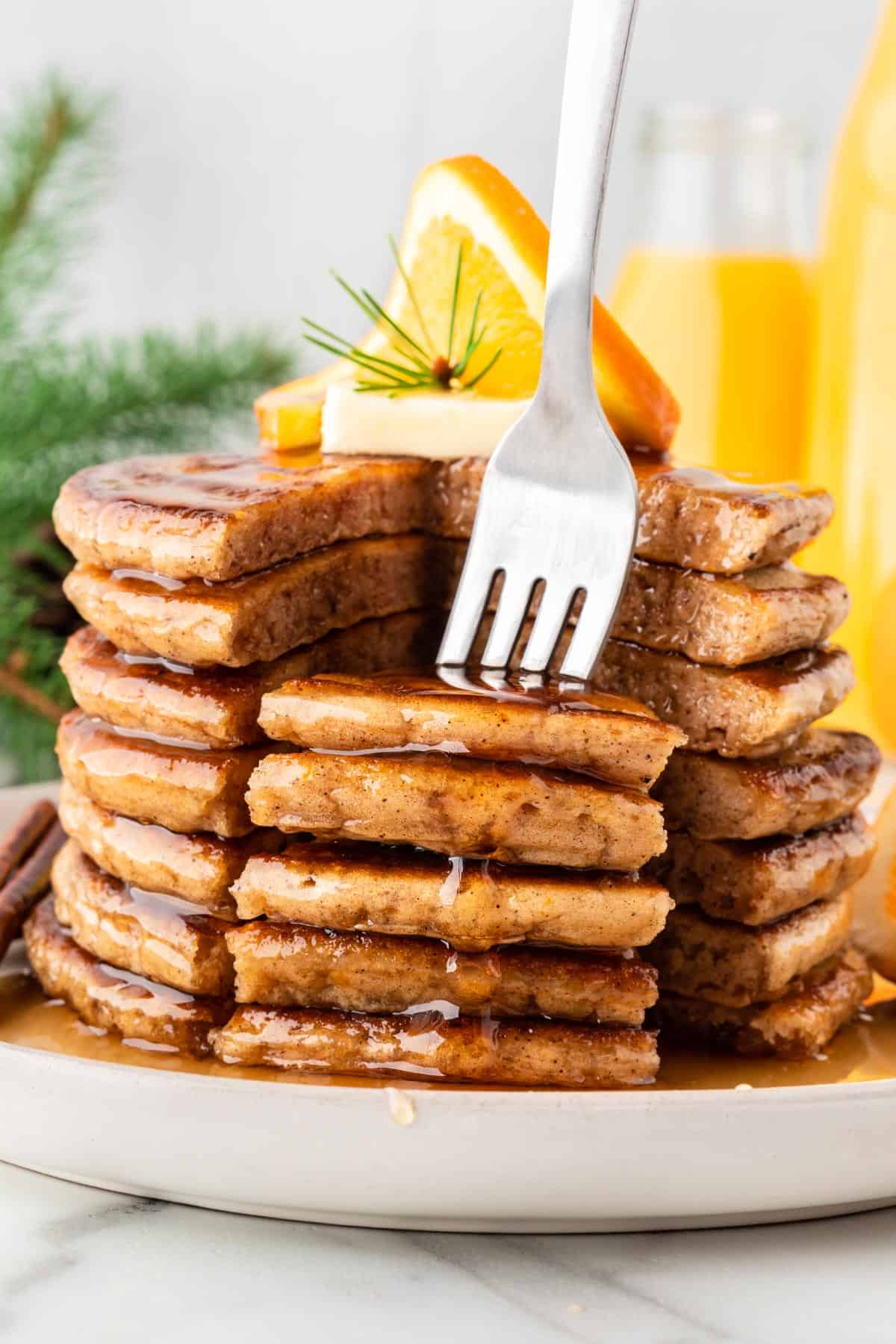 A photo of a fork picking up a bite from a stack of orange pancakes.