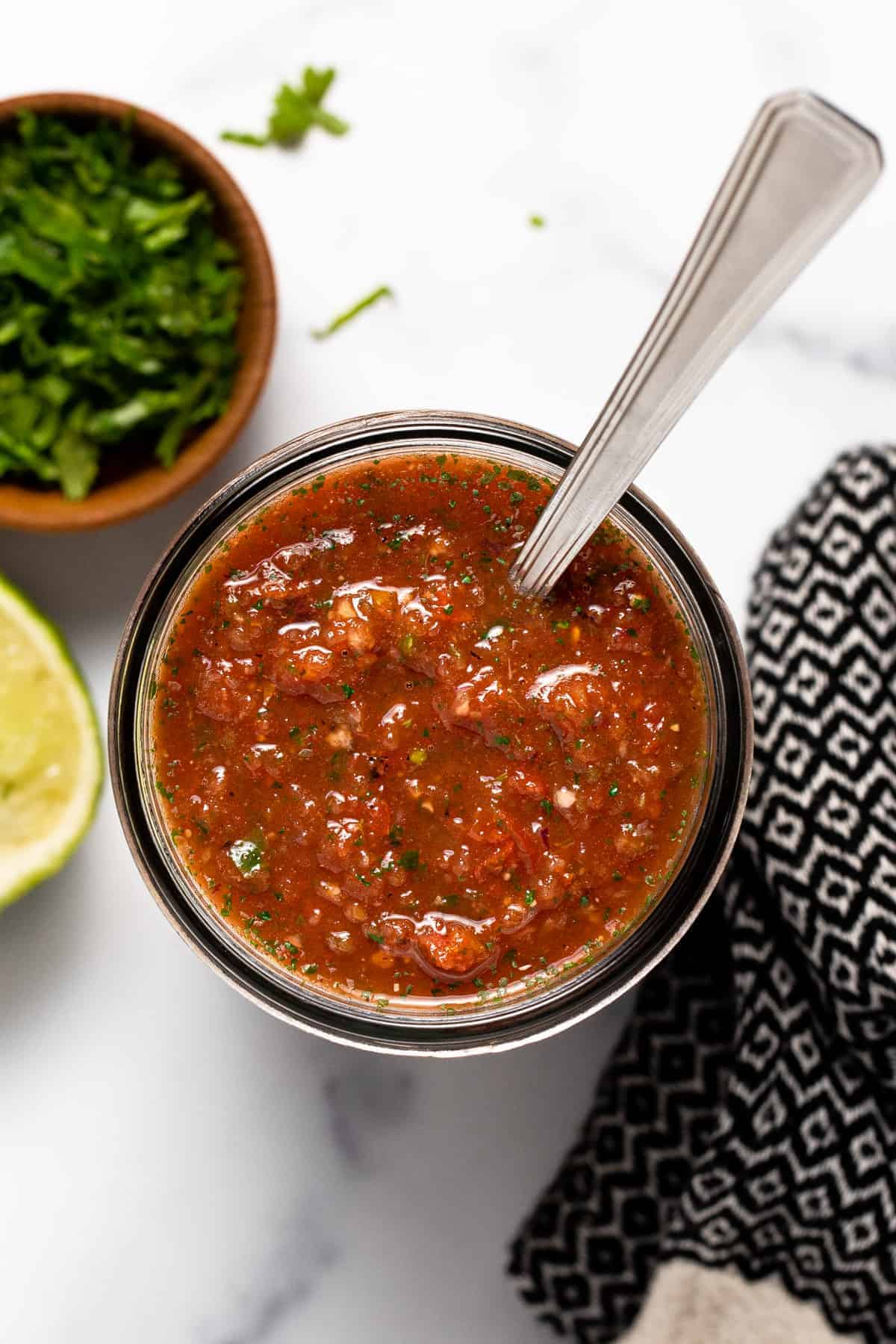 A photo of restaurant style salsa in a jar with a spoon in it.