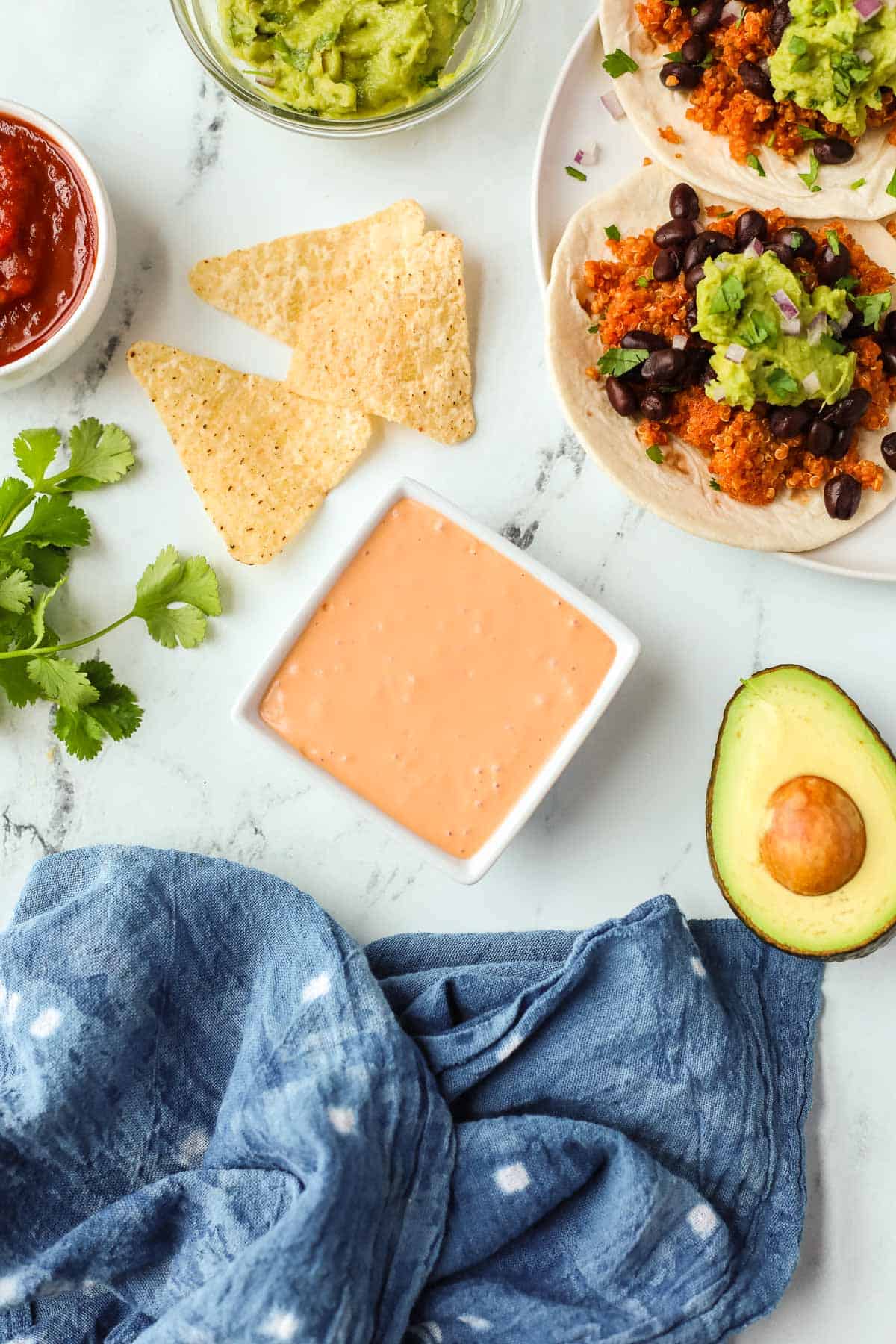 A photo of burrito sauce in a small ramekin with tacos, chips, and avocado on the side.