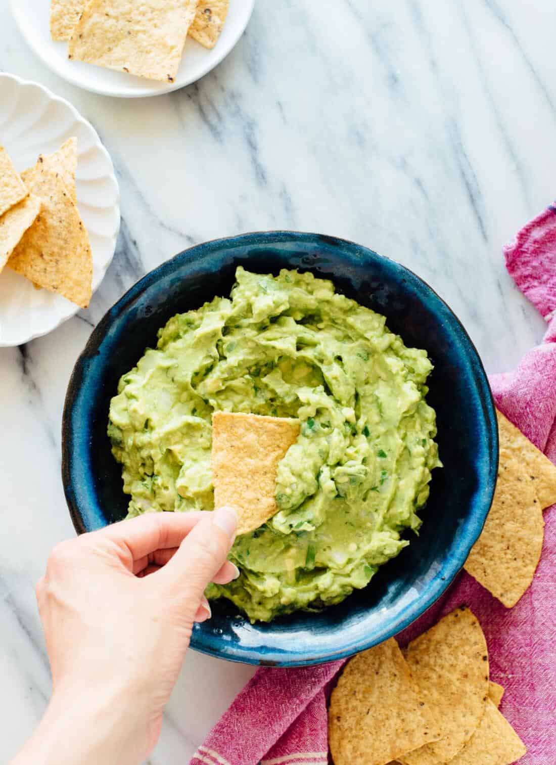 A photo of a person dipping a tortilla chip into a bowl of guacamole.