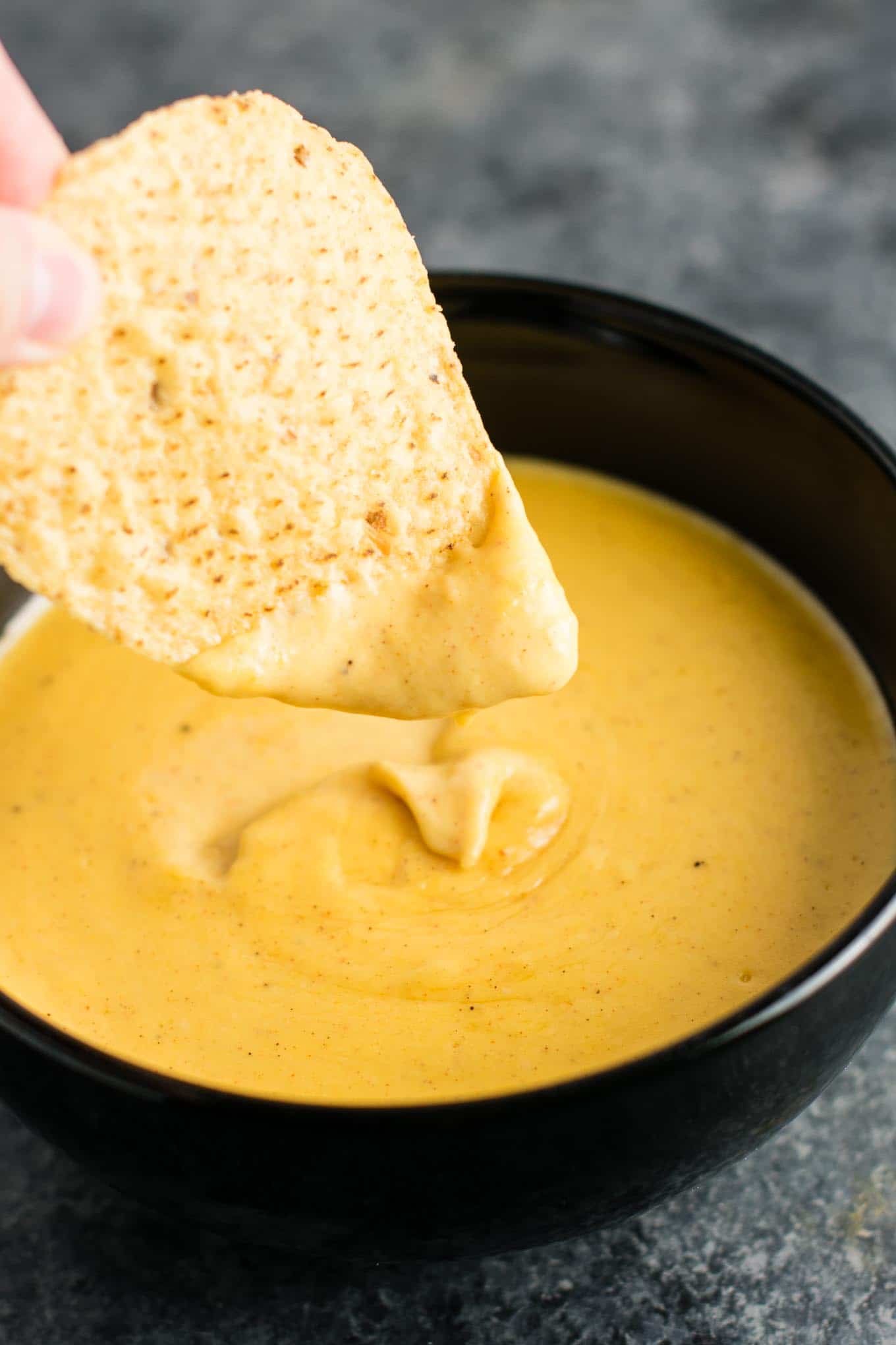 A photo of a tortilla chip being dipped into nacho cheese sauce.