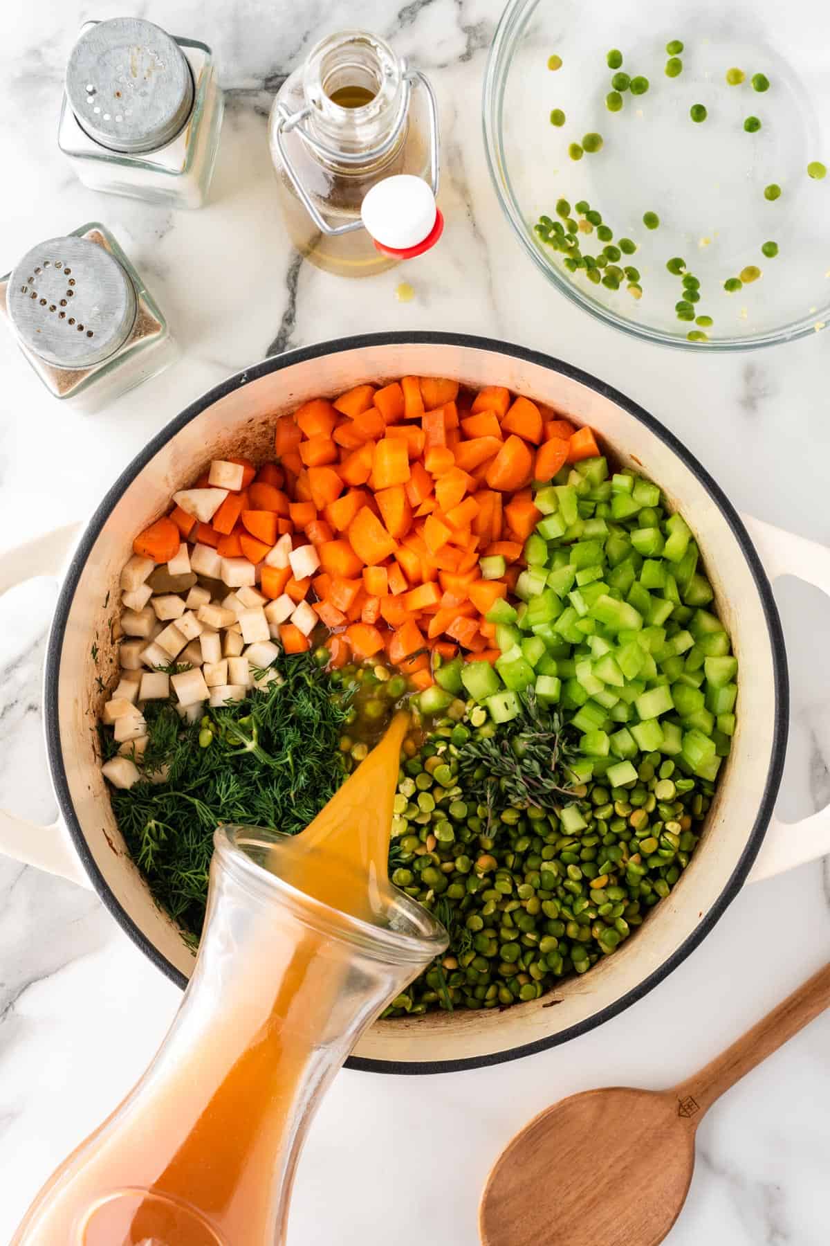 A photo of a pot with split pea soup ingredients and broth being poured into it.