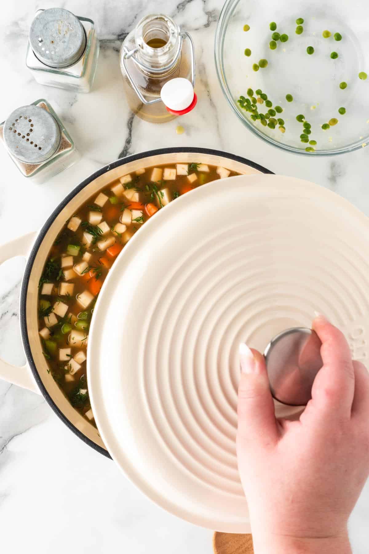 A photo of putting a lid onto a white dutch oven full of soup.
