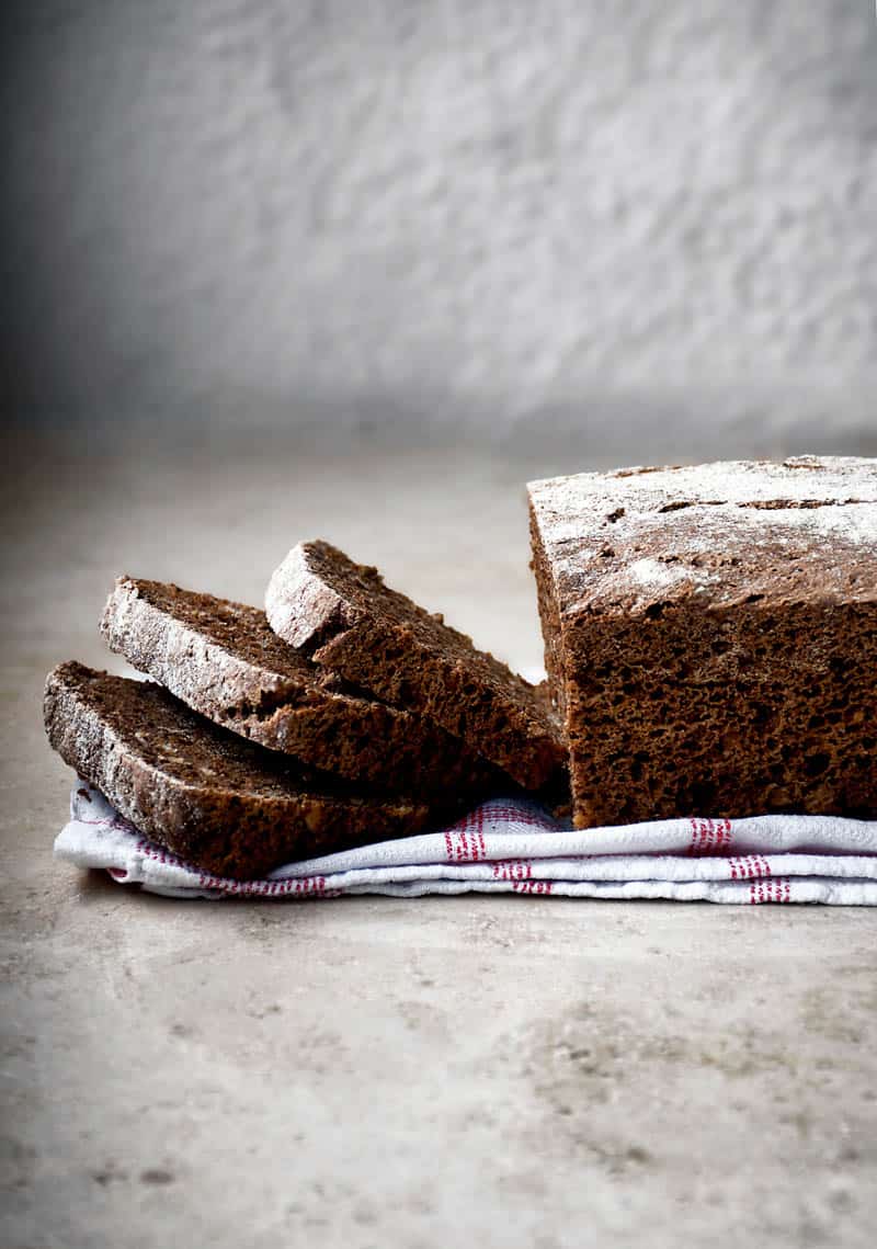 A photo of the side of a loaf of dark rye bread with a few slices already sliced. 
