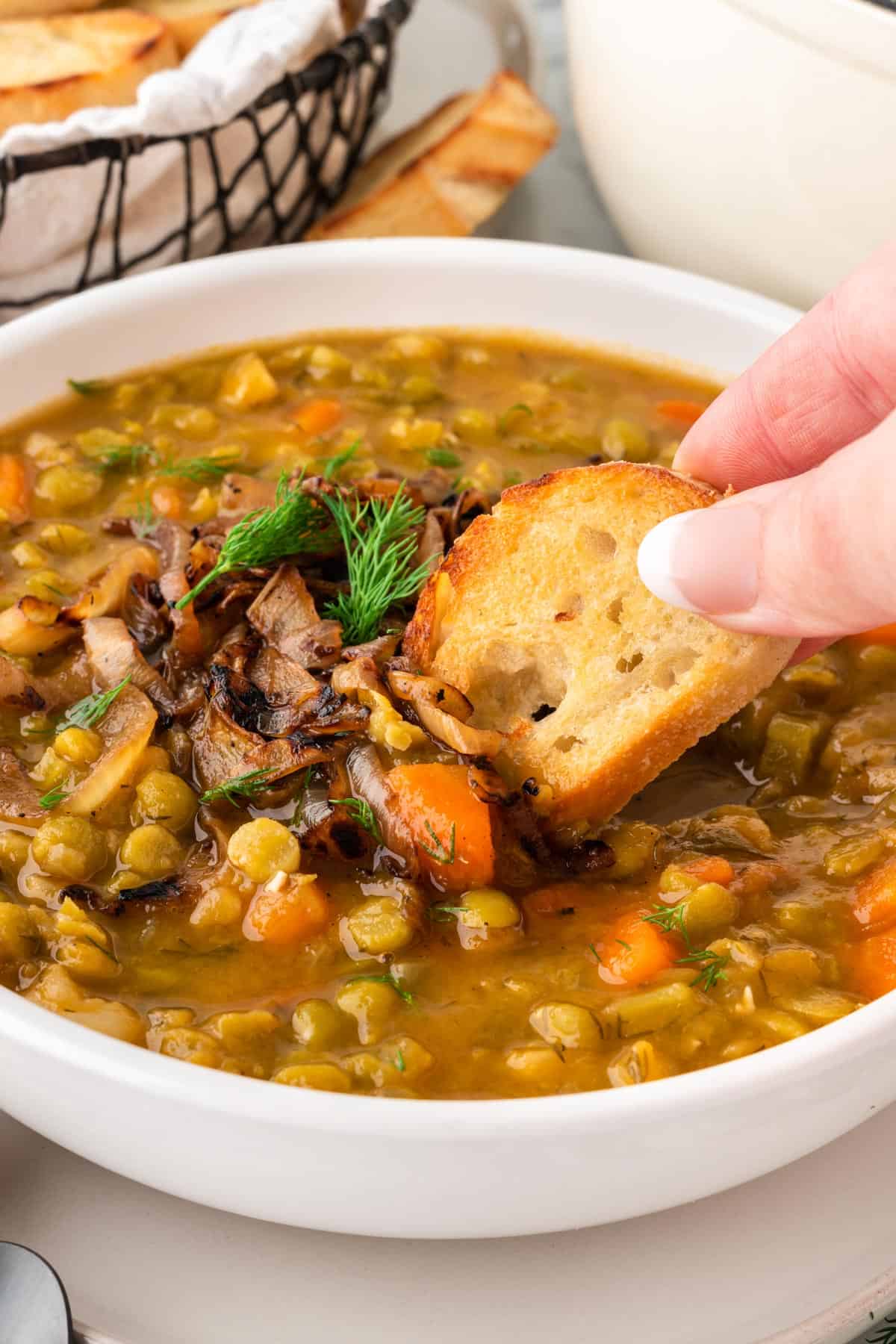 A photo of dipping a baguette into a bowl of split pea soup with burnt onions on top.