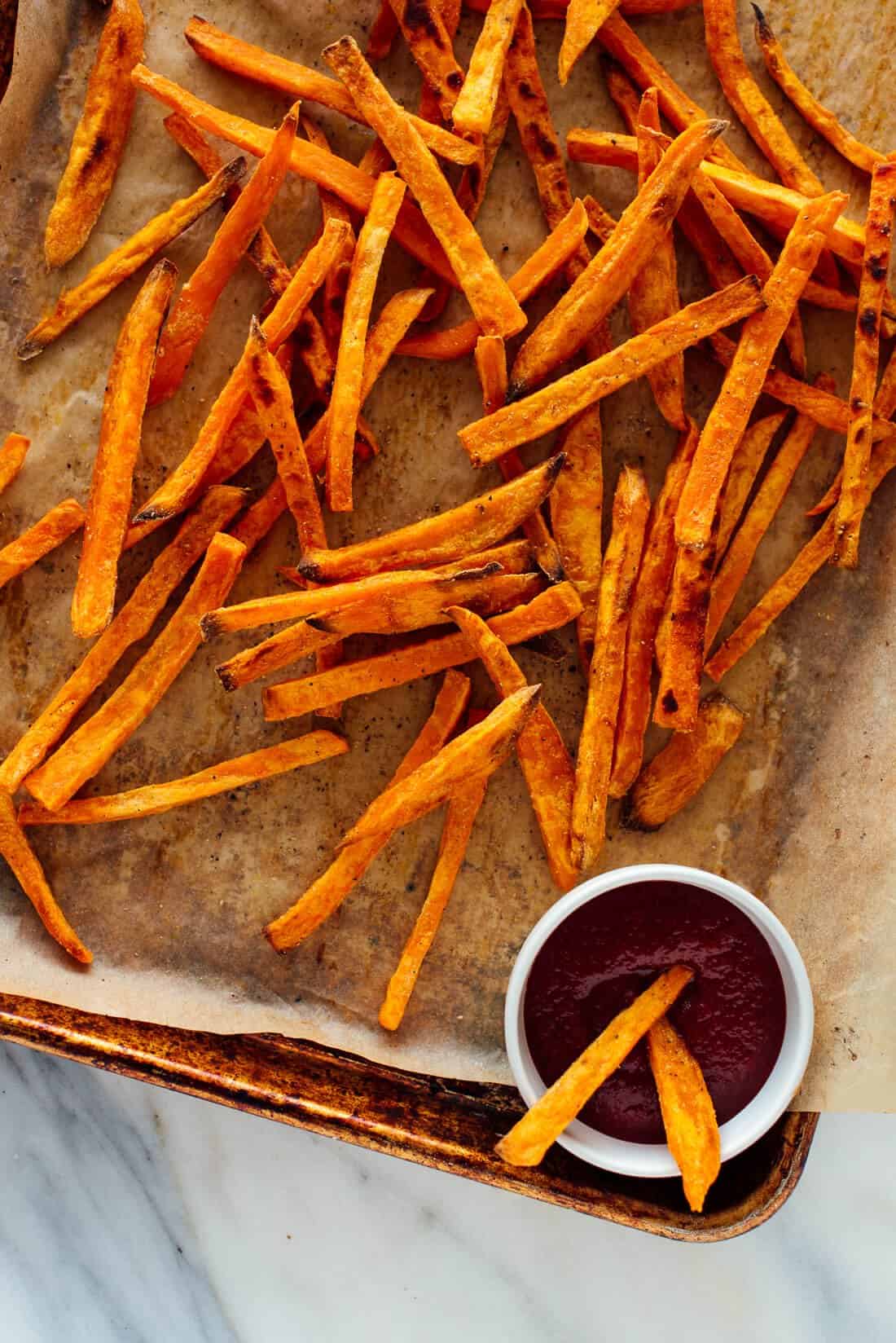 A photo of baked sweet potato fries on a baking sheet with dipping sauce on the side.