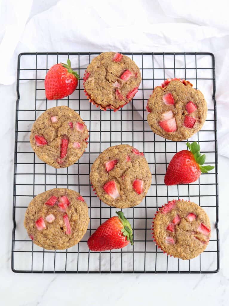 A photo of strawberry oat flour muffins on a cooling rack.