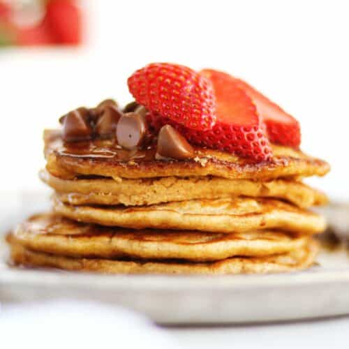A square photo of oat flour pancakes with chocolate chips and strawberries on top.
