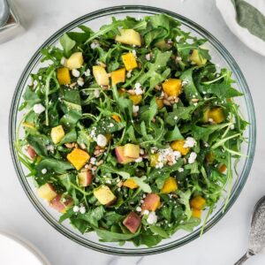 A square photo of a root vegetable and arugula salad in a clear glass bowl.