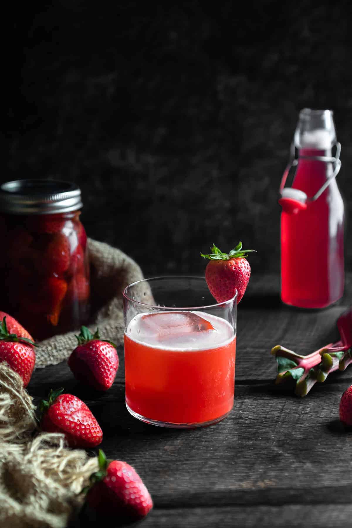 A photo of a strawberry rhubarb whiskey sour with a dark background and a strawberry garnish.