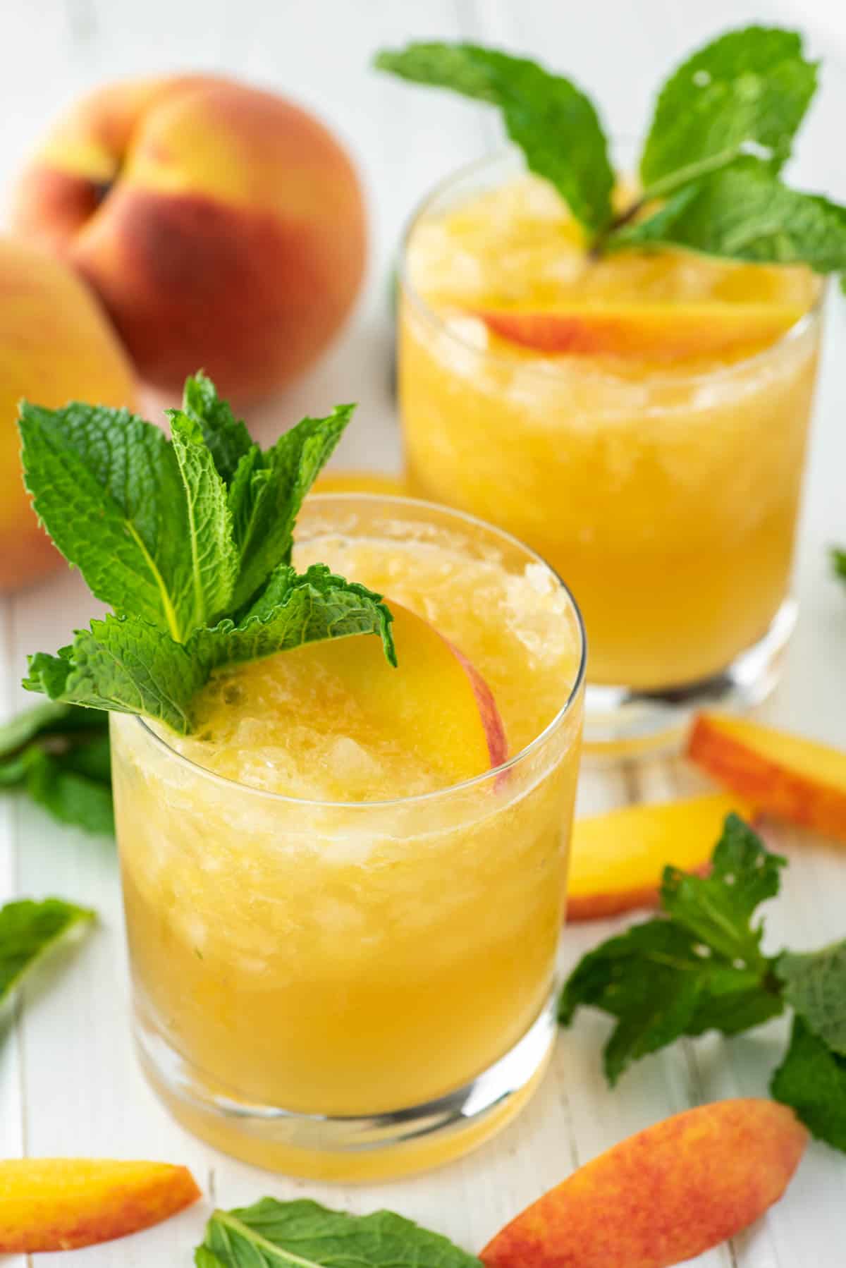 A photo of a bourbon peach smash cocktail with fresh peach and mint garnish.