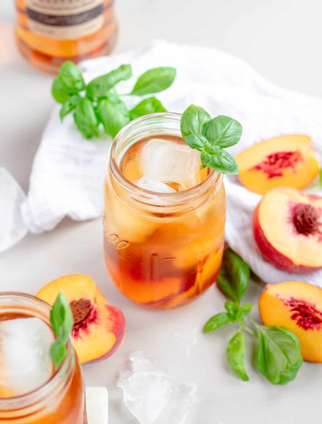 A photo of a bourbon peach iced tea in a mason jar with a basil leaf garnish.