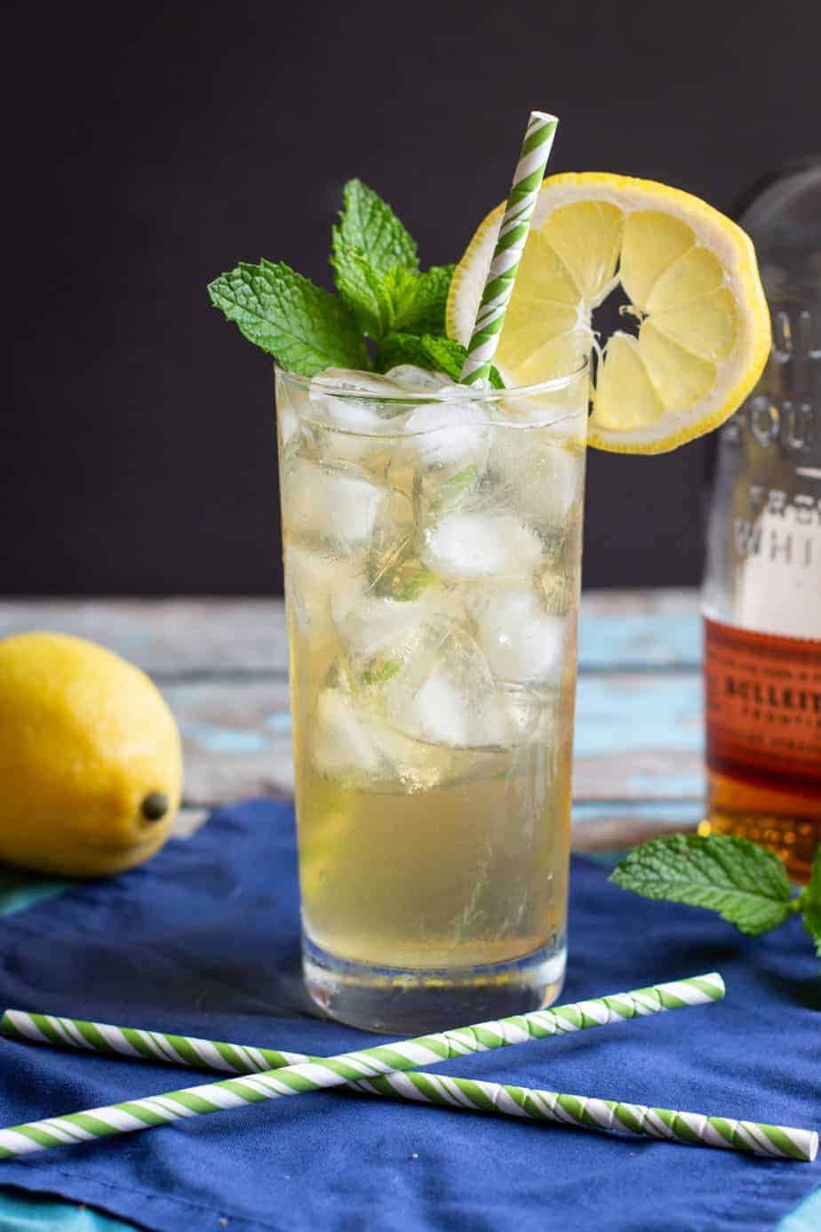 A photo of a Kentucky bourbon lemonade cocktail with a paper straw and lemon and mint garnish.