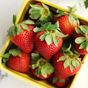 A featured square photo of fresh strawberries in a yellow container for a when is strawberry season post.