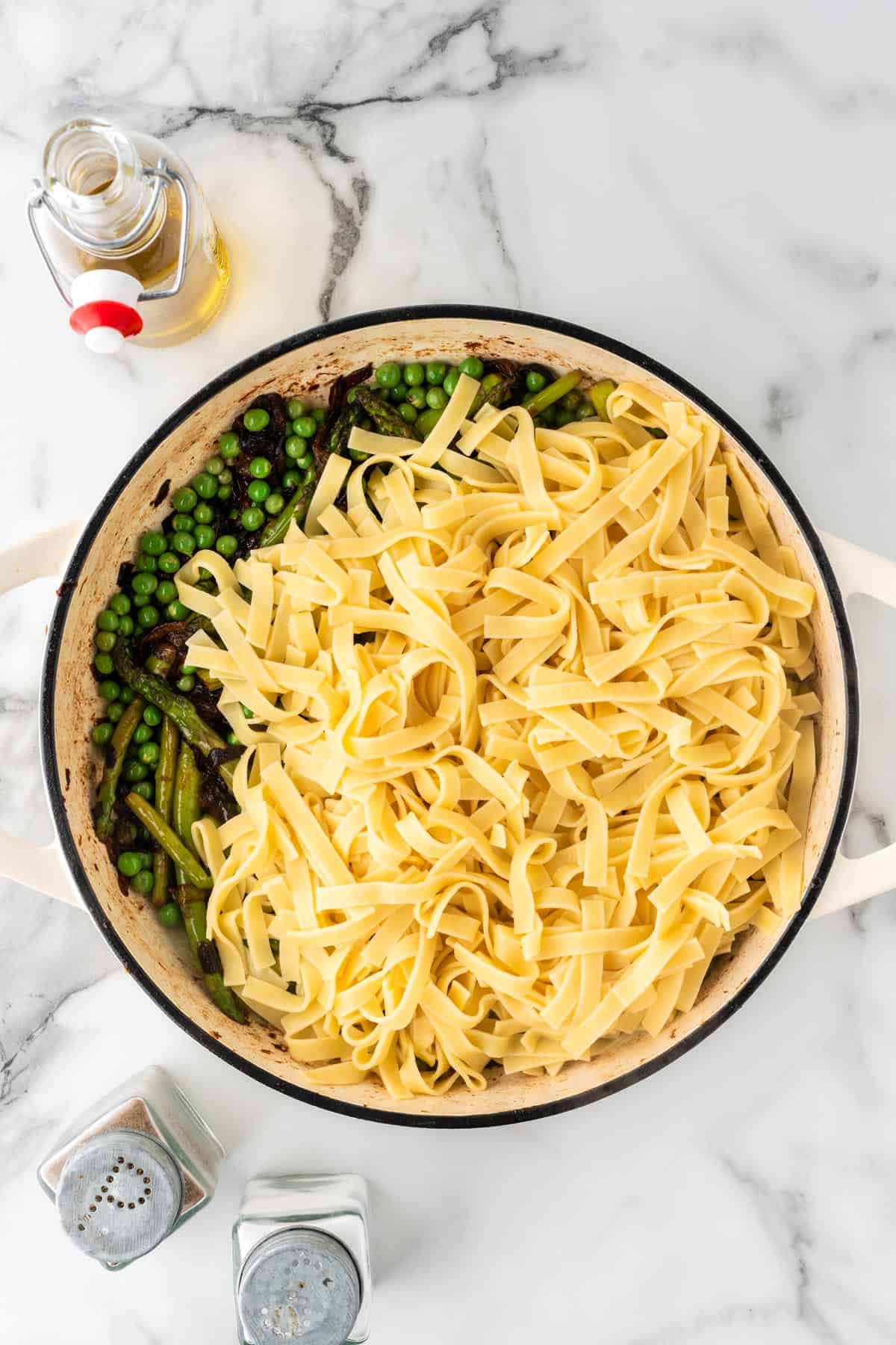 An overhead photo of pasta noodles with spring veggies in a pot.