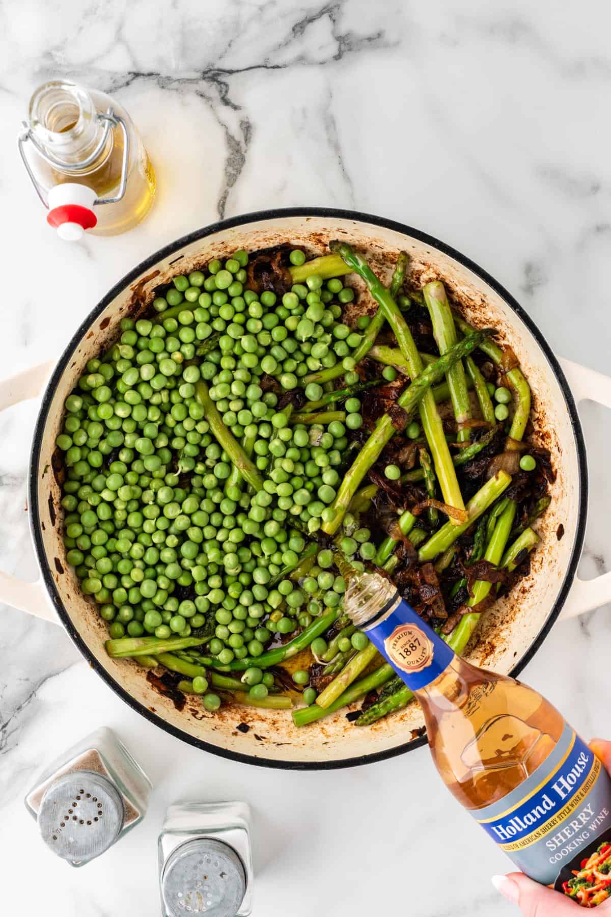 An overhead photo of pouring sherry into a pot of spring vegetables.