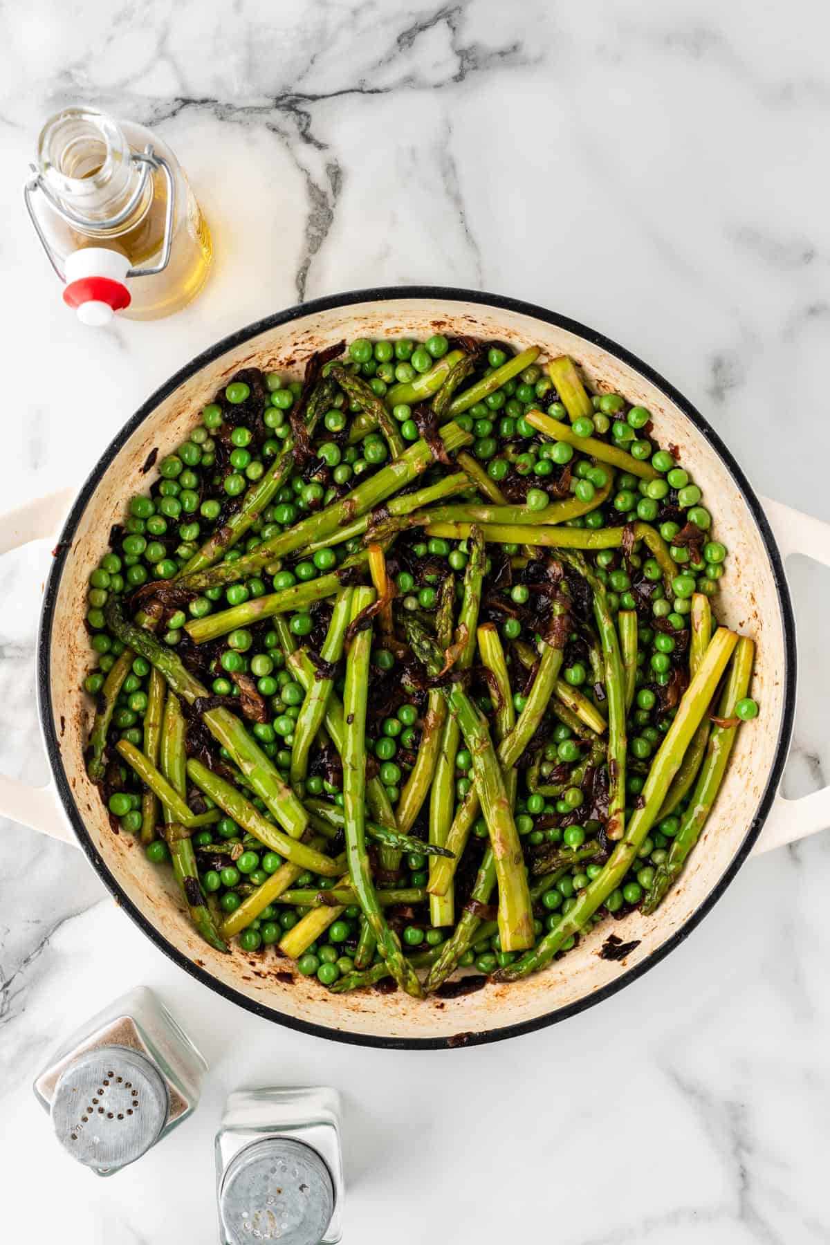 An overhead photo of asparagus, peas, and onions cooking in a pot.